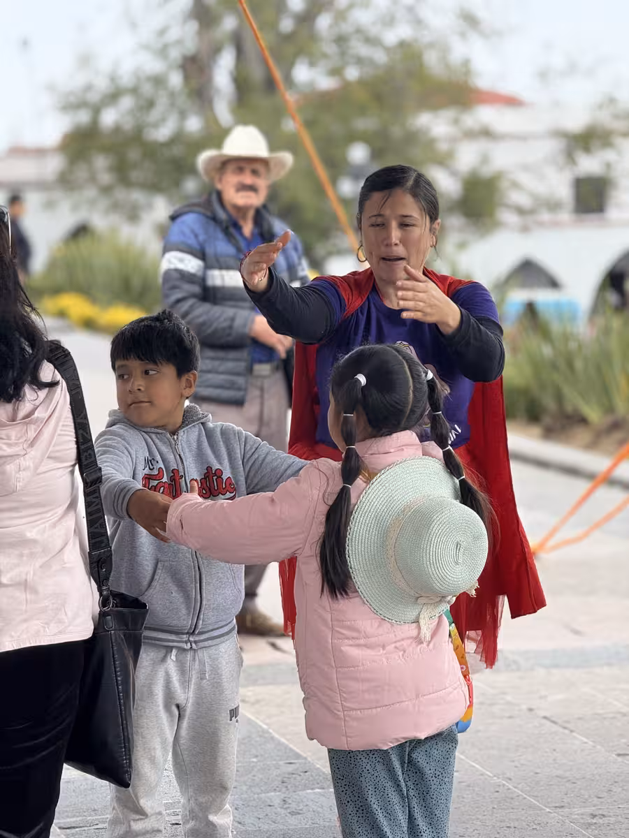 Una tallerista con capa roja interactúa con niños y adultos al aire libre en una plaza pública